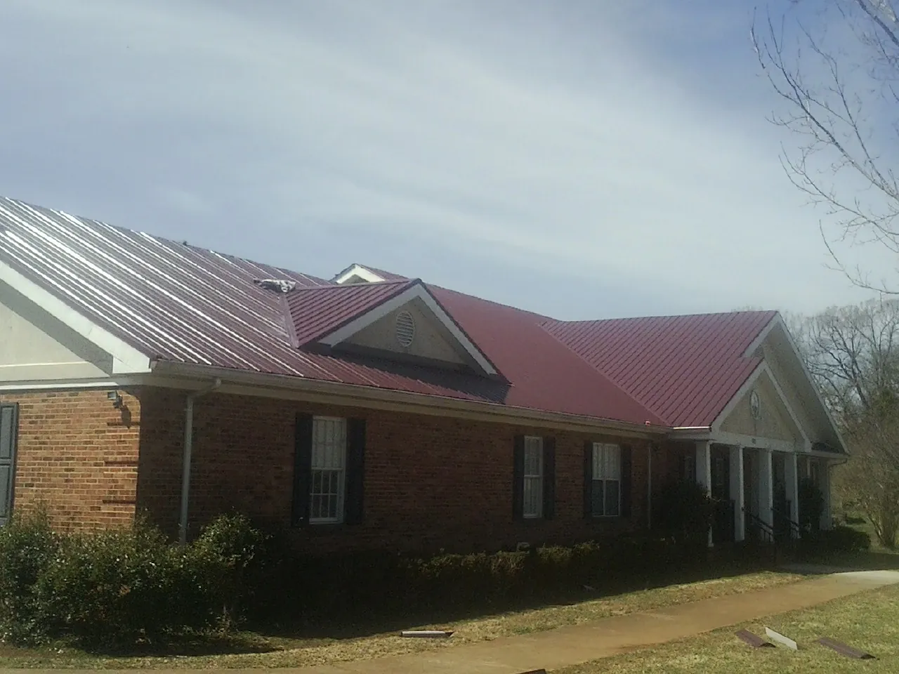 Red metal roof with gabled entries on a long brick building, from a Hail Damage Roof Repair job in Jamaica Plain