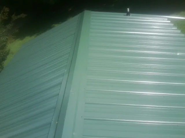 New green metal panels meeting at the ridge of a roof — Flat Roof Repair work by our crew in Jamaica Plain