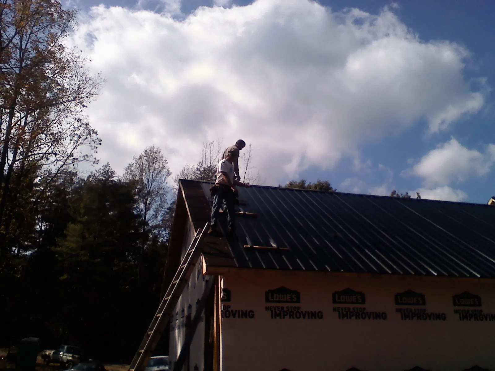 Roofer fastening dark metal panels high against a cloudy sky, from a Roof Inspection job in Jamaica Plain