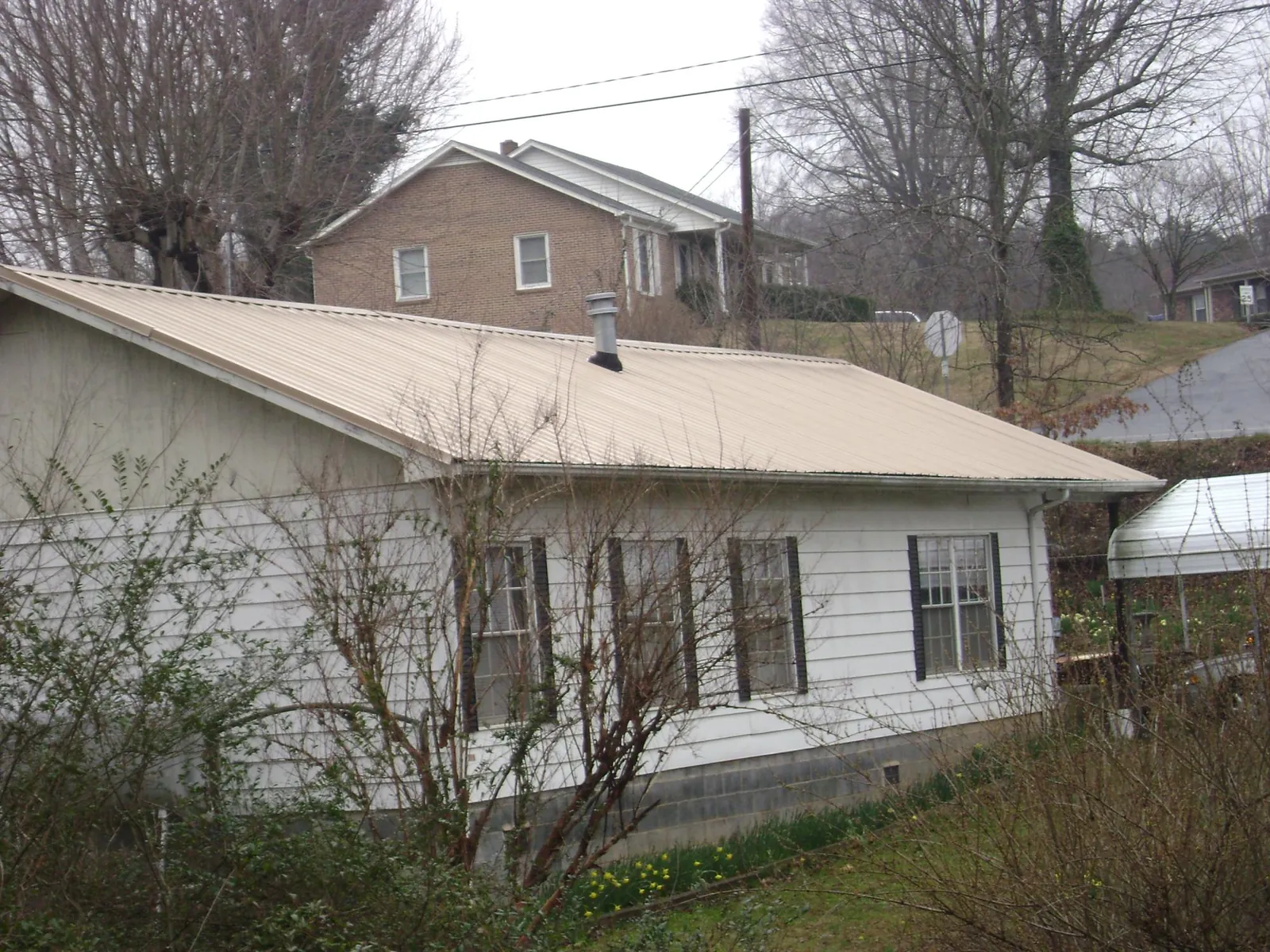 Tan metal roof on a white sided house set into a hillside — Commercial Roofing by Roofing Brothers in Jamaica Plain